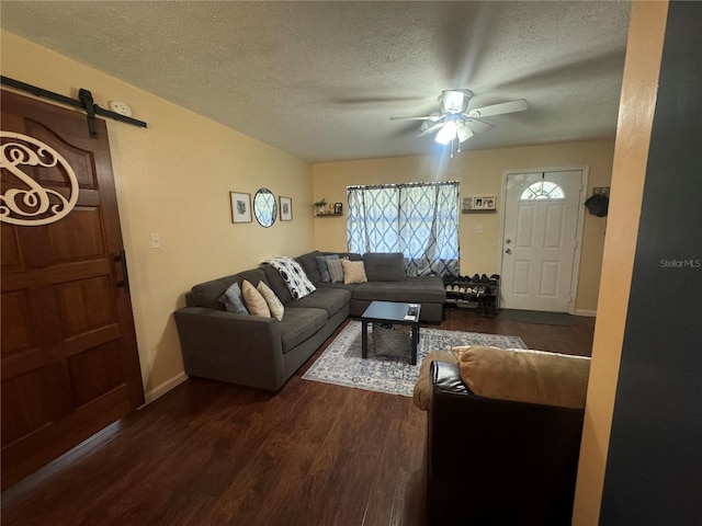 living room featuring hardwood / wood-style flooring, a textured ceiling, a barn door, and ceiling fan