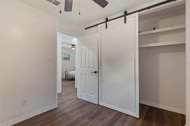 unfurnished bedroom featuring a closet, ceiling fan, dark wood-type flooring, and a barn door