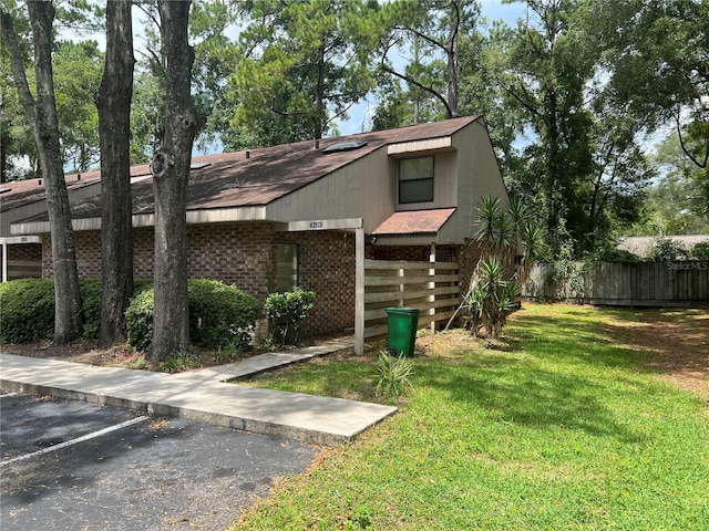 view of home's exterior with uncovered parking, fence, a lawn, and brick siding