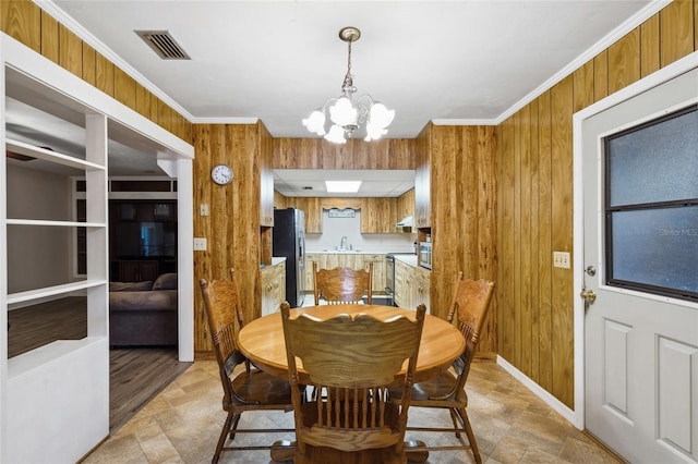 dining space featuring wood walls, an inviting chandelier, sink, crown molding, and light wood-type flooring