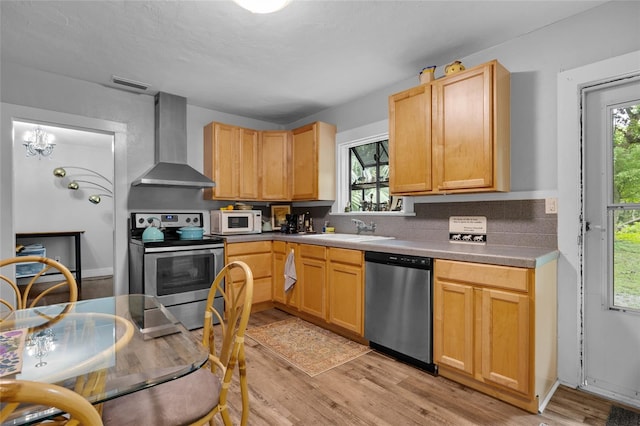 kitchen with wall chimney exhaust hood, light hardwood / wood-style flooring, appliances with stainless steel finishes, and light brown cabinets