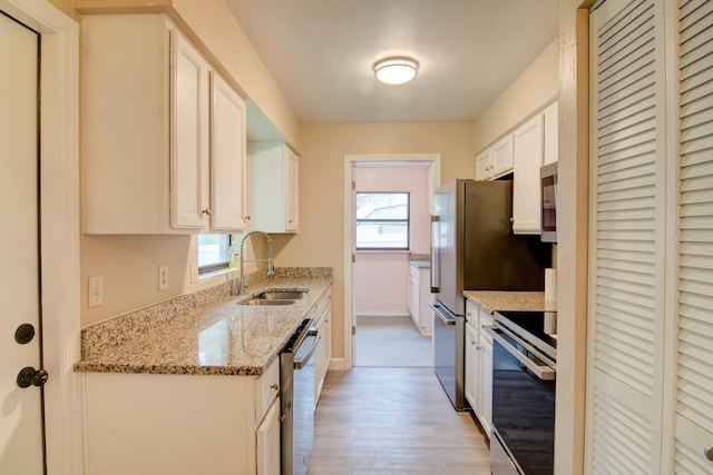 kitchen with sink, appliances with stainless steel finishes, light hardwood / wood-style flooring, light stone countertops, and white cabinetry