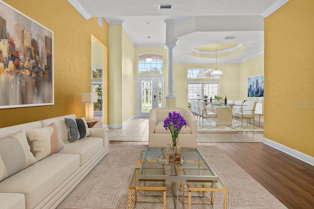 living room with french doors, an inviting chandelier, decorative columns, ornamental molding, and light wood-type flooring