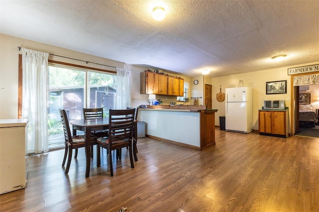 kitchen with kitchen peninsula, a textured ceiling, white fridge, and dark hardwood / wood-style floors