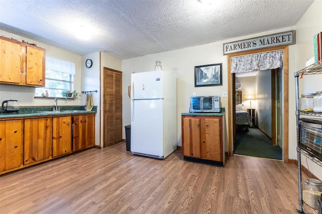 kitchen featuring sink, wood-type flooring, white refrigerator, and a textured ceiling