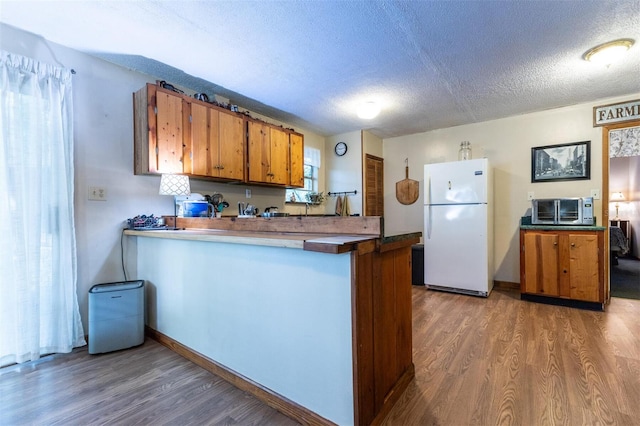 kitchen with kitchen peninsula, white refrigerator, a textured ceiling, and dark wood-type flooring