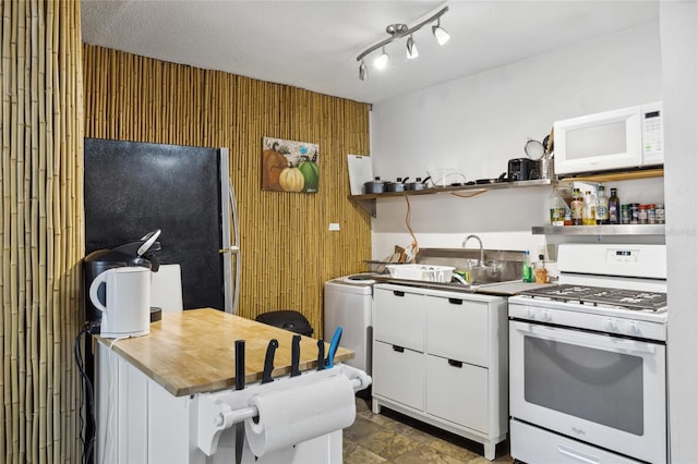 kitchen featuring dark tile patterned floors, rail lighting, sink, white cabinets, and white appliances