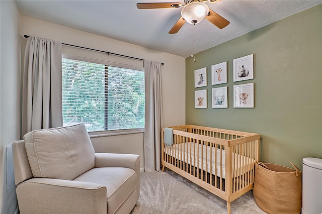 carpeted bedroom with ceiling fan and a crib