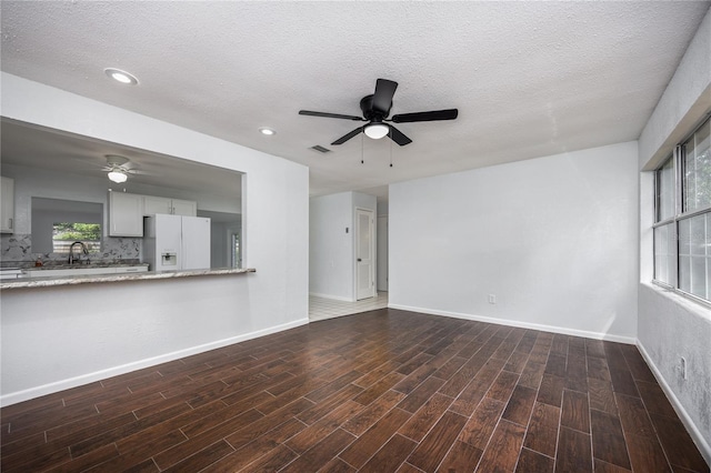 unfurnished living room with a wealth of natural light, dark wood-type flooring, ceiling fan, and a textured ceiling