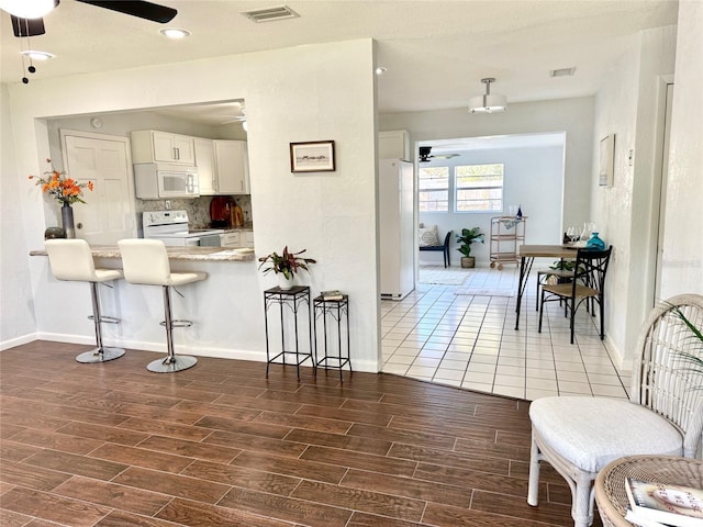 kitchen with white appliances, wood tiled floor, visible vents, and a breakfast bar