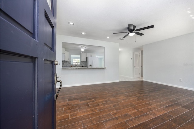 unfurnished living room with ceiling fan, baseboards, dark wood finished floors, and a textured ceiling