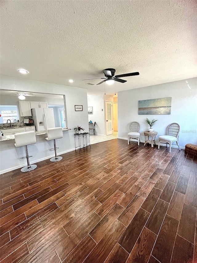 interior space with a textured ceiling, wood finish floors, a ceiling fan, and baseboards