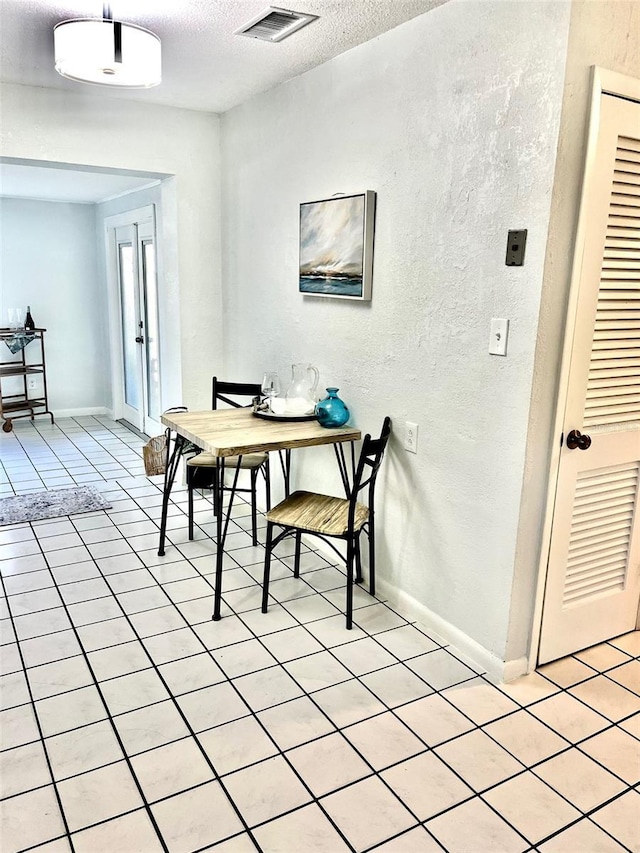 dining area with a textured ceiling, a textured wall, light tile patterned flooring, visible vents, and baseboards