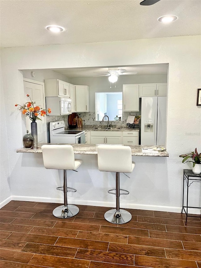 kitchen featuring white appliances, wood tiled floor, a kitchen bar, and a sink