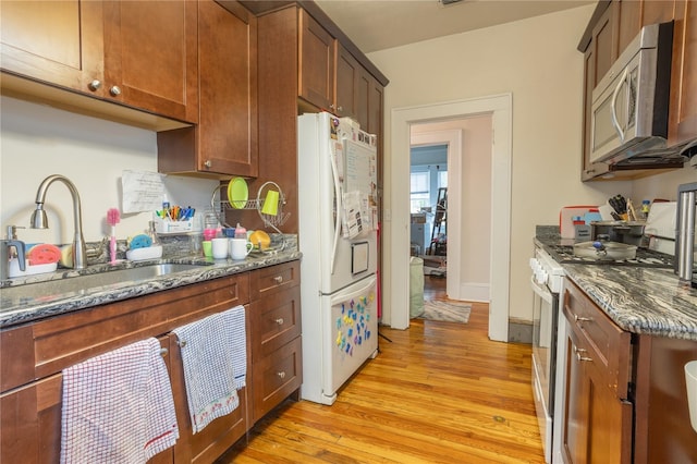 kitchen featuring sink, white appliances, light hardwood / wood-style floors, and dark stone countertops