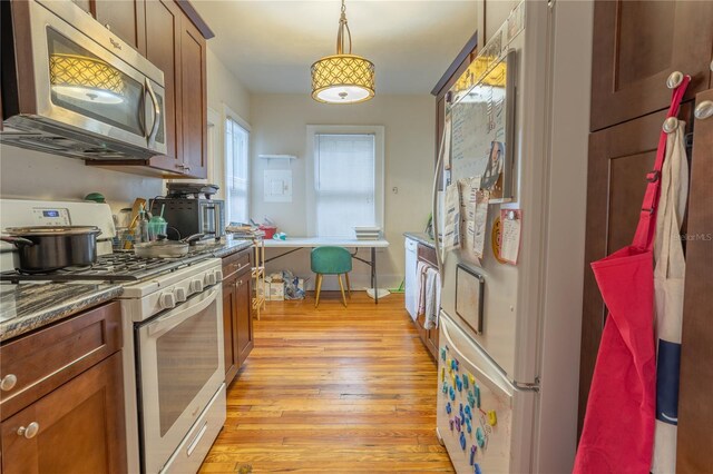 kitchen featuring pendant lighting, light hardwood / wood-style floors, white appliances, and dark stone countertops