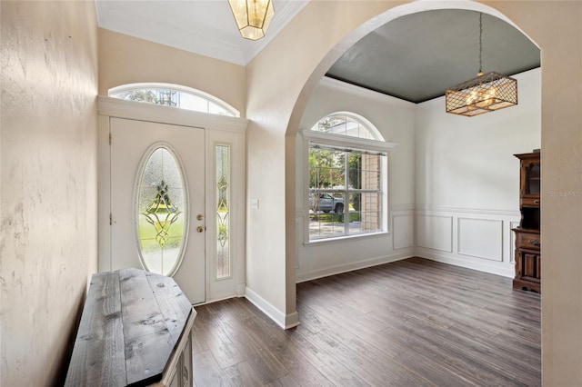 foyer with dark wood-type flooring, ornamental molding, and a chandelier