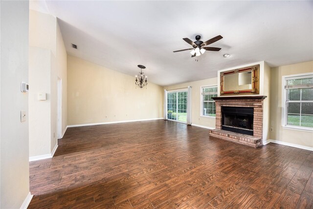 unfurnished living room with a healthy amount of sunlight, vaulted ceiling, a brick fireplace, ceiling fan with notable chandelier, and dark hardwood / wood-style flooring