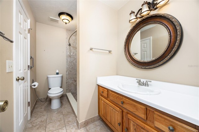 bathroom featuring tile patterned flooring, toilet, a tile shower, and vanity