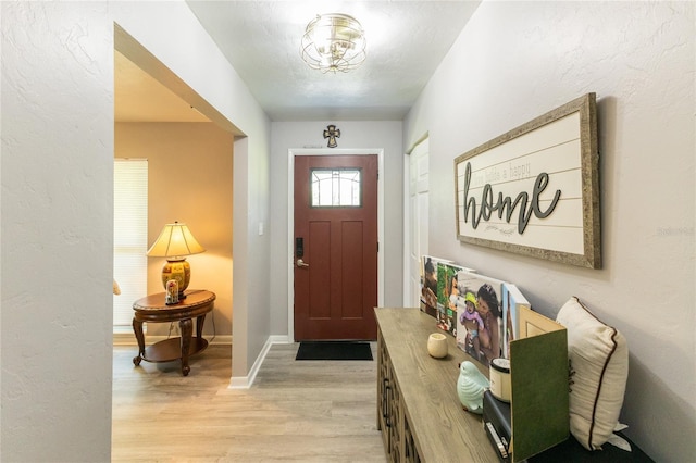 foyer entrance with light wood-style floors, baseboards, a textured ceiling, and a textured wall