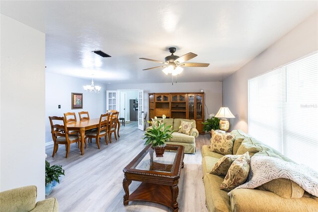 living room with ceiling fan with notable chandelier, light wood-style flooring, visible vents, and baseboards