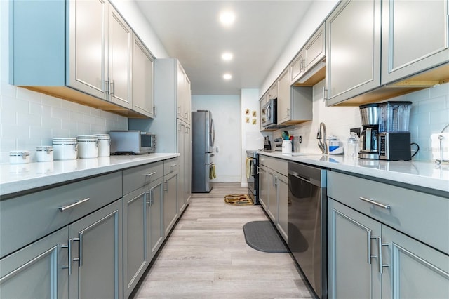 kitchen with light wood finished floors, stainless steel appliances, gray cabinets, and light countertops