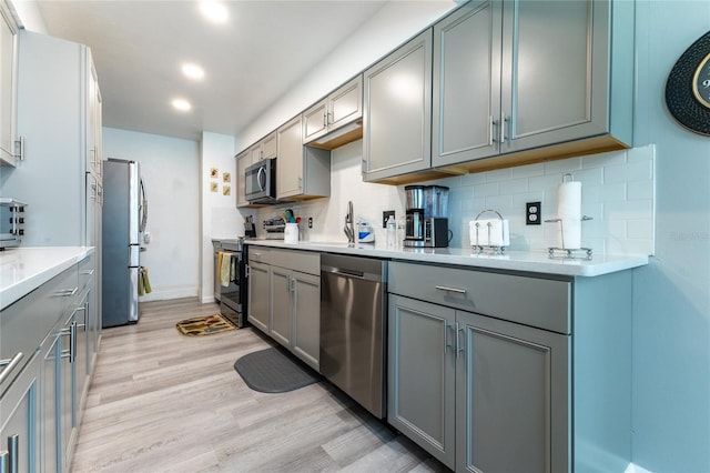 kitchen featuring decorative backsplash, light wood-style flooring, gray cabinets, stainless steel appliances, and light countertops