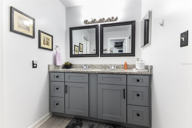 bathroom with wood finished floors, a sink, baseboards, and double vanity