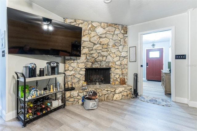 living room with baseboards, a stone fireplace, ornamental molding, and light wood-style floors