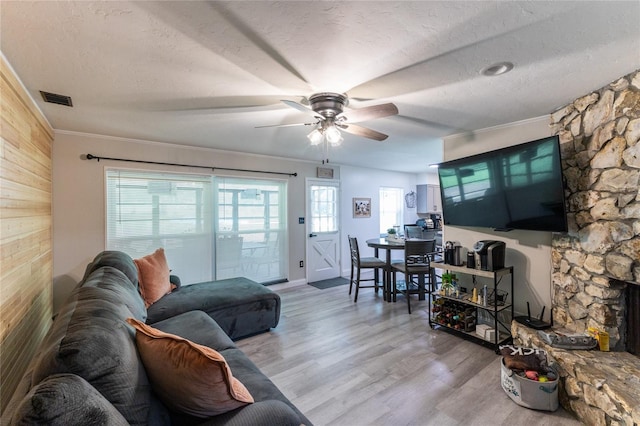 living room featuring a textured ceiling, a fireplace, visible vents, and light wood-style floors