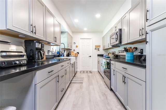 kitchen featuring light wood-style flooring, recessed lighting, a sink, appliances with stainless steel finishes, and dark countertops