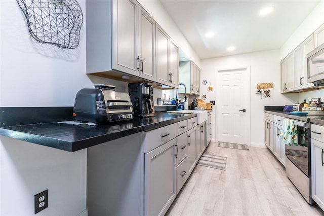 kitchen featuring recessed lighting, a sink, stainless steel electric stove, light wood finished floors, and dark countertops