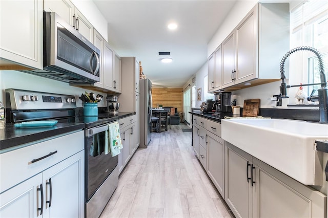 kitchen featuring a sink, white cabinetry, appliances with stainless steel finishes, light wood finished floors, and dark countertops