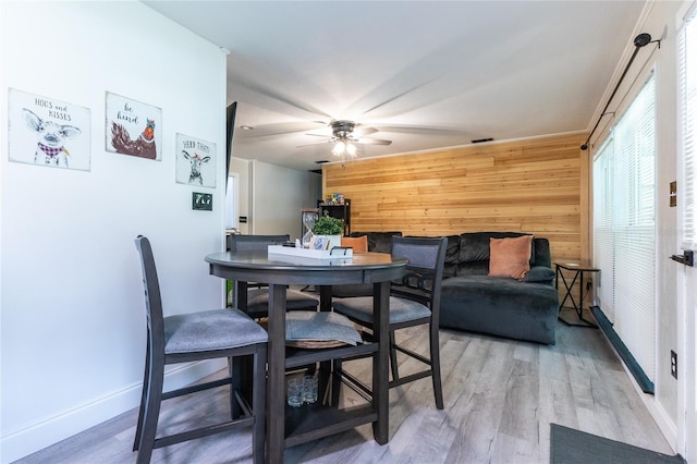 dining area featuring visible vents, ceiling fan, wooden walls, and wood finished floors