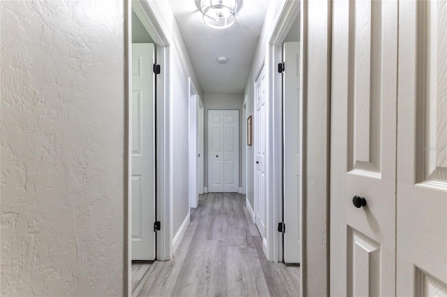 hall with a textured wall, light wood-type flooring, and baseboards