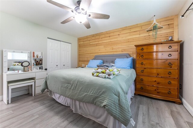 bedroom featuring ceiling fan, a closet, light wood-style flooring, and wooden walls