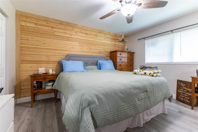 bedroom with wood walls, light wood-style flooring, and ceiling fan