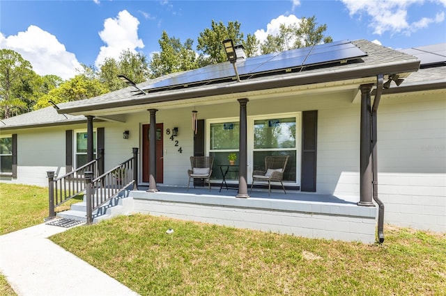 single story home featuring solar panels, a porch, roof with shingles, and a front yard