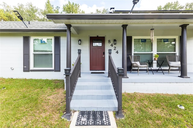 view of exterior entry with covered porch, roof with shingles, and a lawn