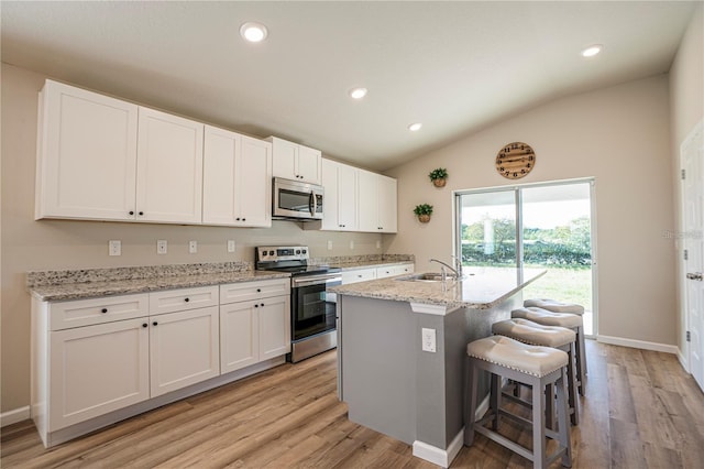 kitchen featuring an island with sink, light stone counters, stainless steel appliances, white cabinetry, and a sink