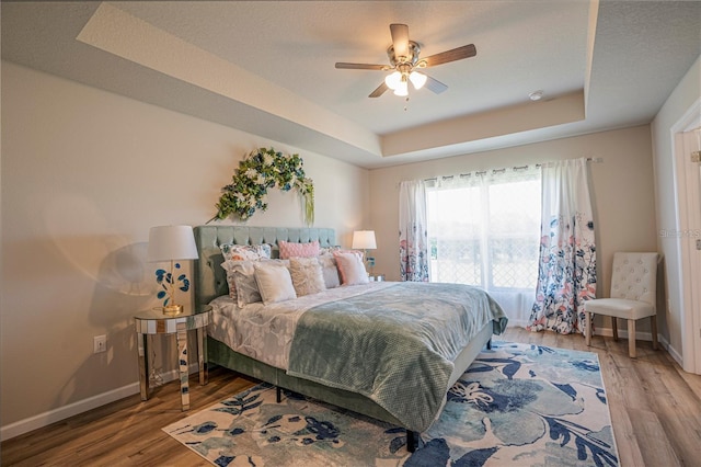 bedroom with a tray ceiling, baseboards, and wood finished floors