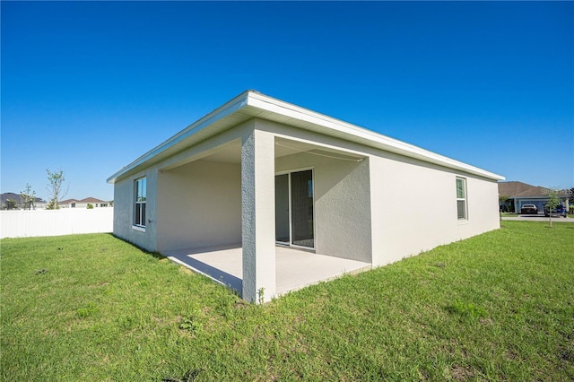 back of property featuring stucco siding, a patio area, fence, and a yard