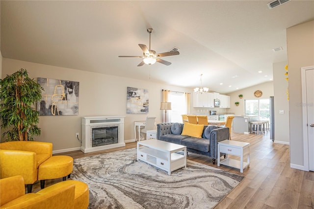 living room featuring lofted ceiling, light wood-style floors, plenty of natural light, and a glass covered fireplace