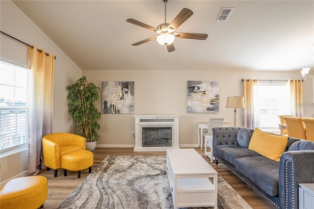 living room with ceiling fan, wood finished floors, visible vents, baseboards, and a glass covered fireplace