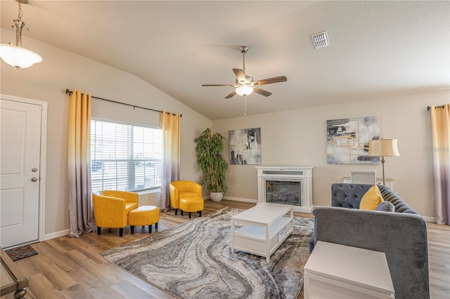 living area featuring light wood-type flooring, a fireplace, vaulted ceiling, and visible vents