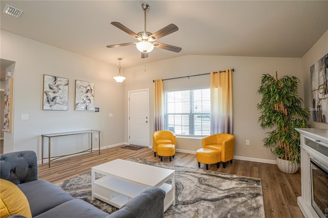 living area with visible vents, a glass covered fireplace, ceiling fan, dark wood-type flooring, and vaulted ceiling