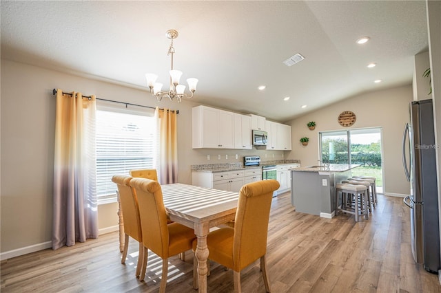 dining space with lofted ceiling, light wood-style flooring, visible vents, and an inviting chandelier