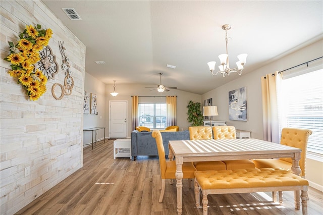 dining area featuring ceiling fan with notable chandelier, visible vents, vaulted ceiling, and wood finished floors