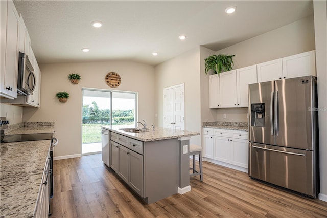 kitchen with a center island with sink, light stone countertops, stainless steel appliances, a kitchen bar, and white cabinetry