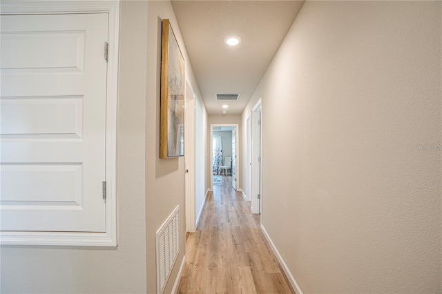 corridor with light wood finished floors, baseboards, and visible vents